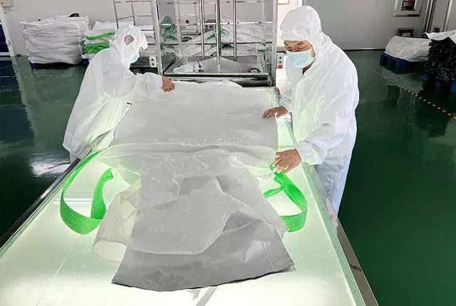 Workers in clean room suits handling a food grade bulk bag under controlled lighting