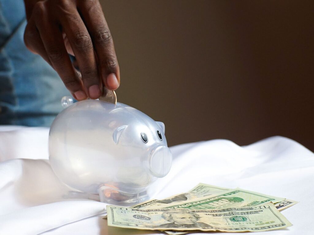 Hand placing a coin into a piggy bank next to dollar bills